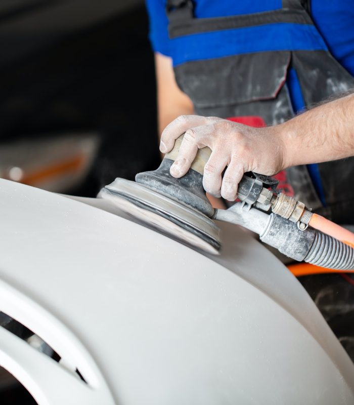 A man who sanding with a grinder and prepares the paint for the car in a car service.