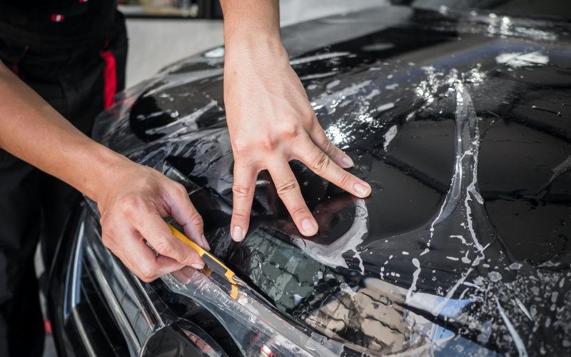 Hands installs car paint protection film.