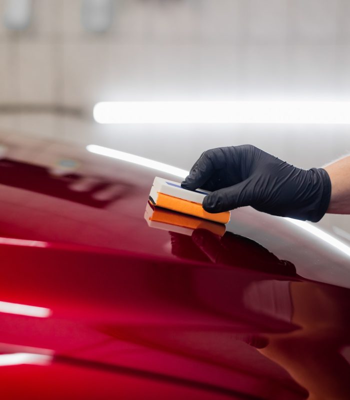 Man worker of car detailing studio applying ceramic coating on car paint with sponge applicator