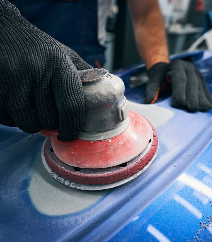 Sander grinding painted bumper in car workshop